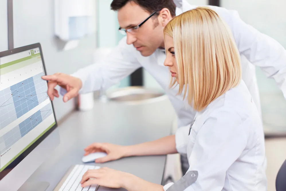 Two medical professionals analyzing data on a computer screen, discussing common denials in medical billing.